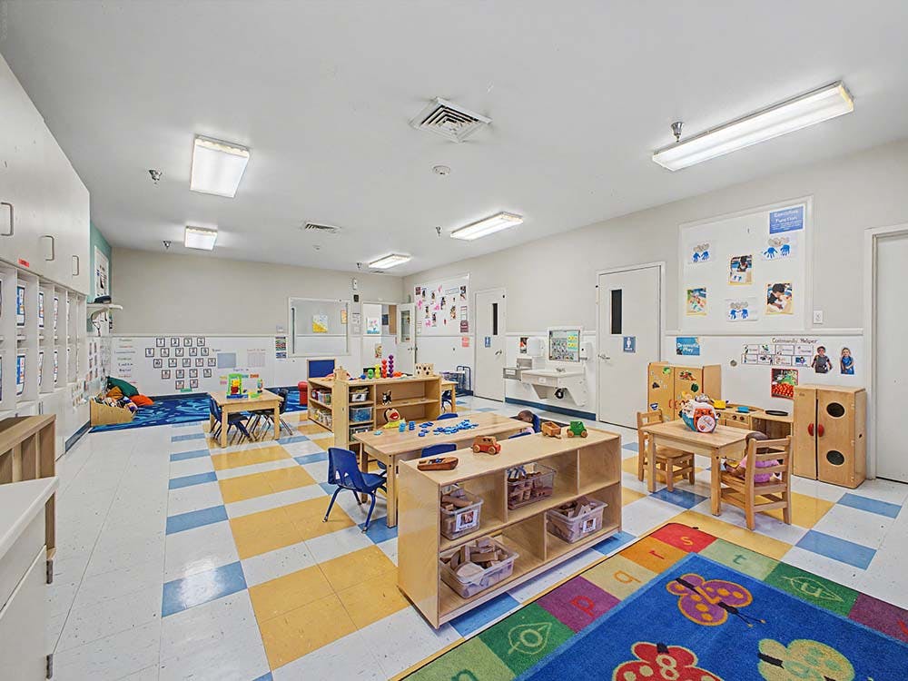 Empty classroom with small tables, chairs, and shelves