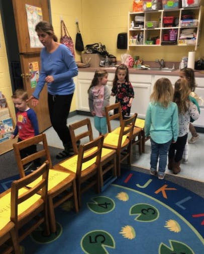Adult and children in a classroom with chairs lined up
