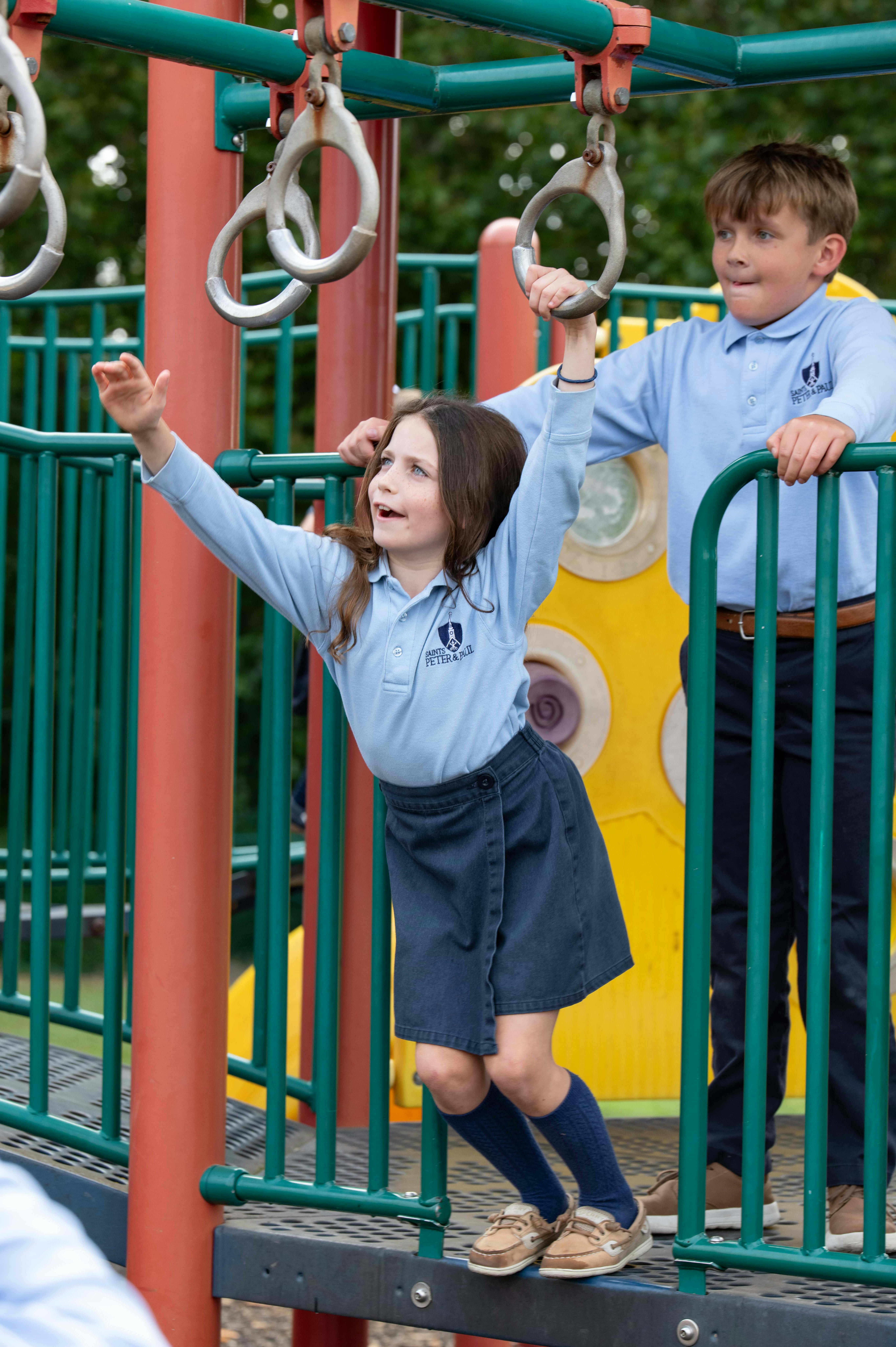 Two children on a playground structure, one reaching for monkey bars