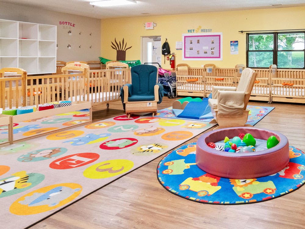 Daycare room with multiple cribs, two rocking chairs, and colorful play mats