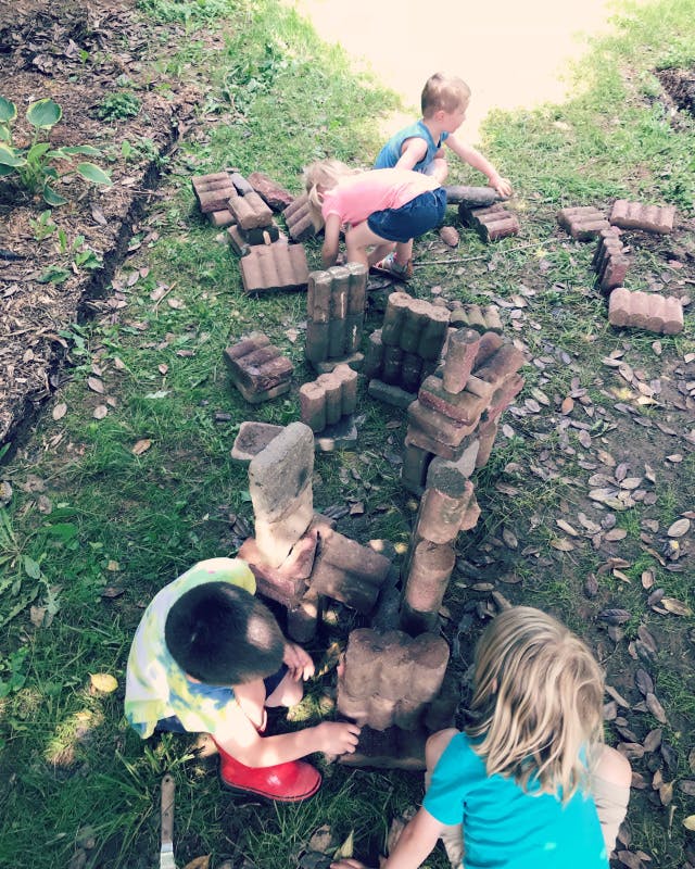 Three children playing with bricks on the grass