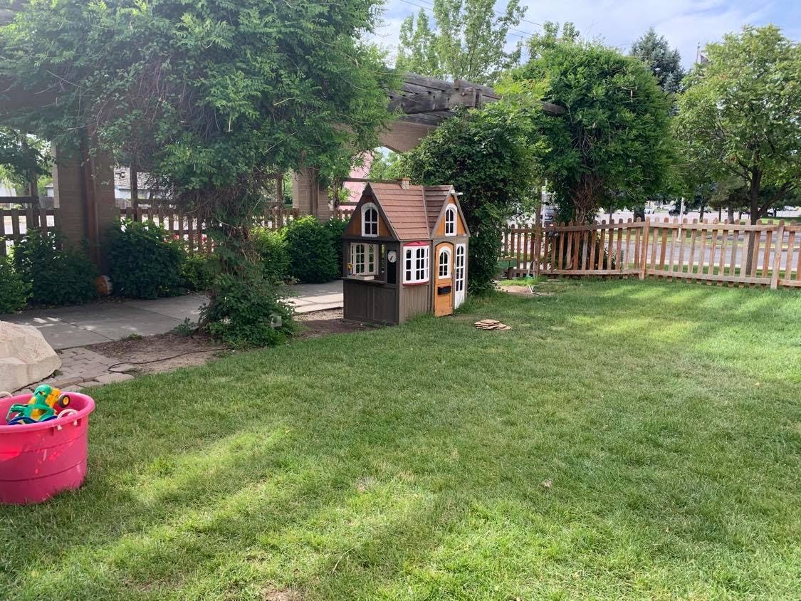 Playhouse in a grassy yard with a fence and trees