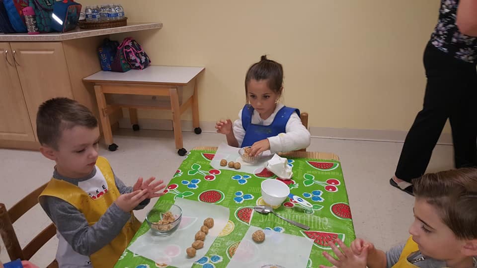 Children making small round objects at a table