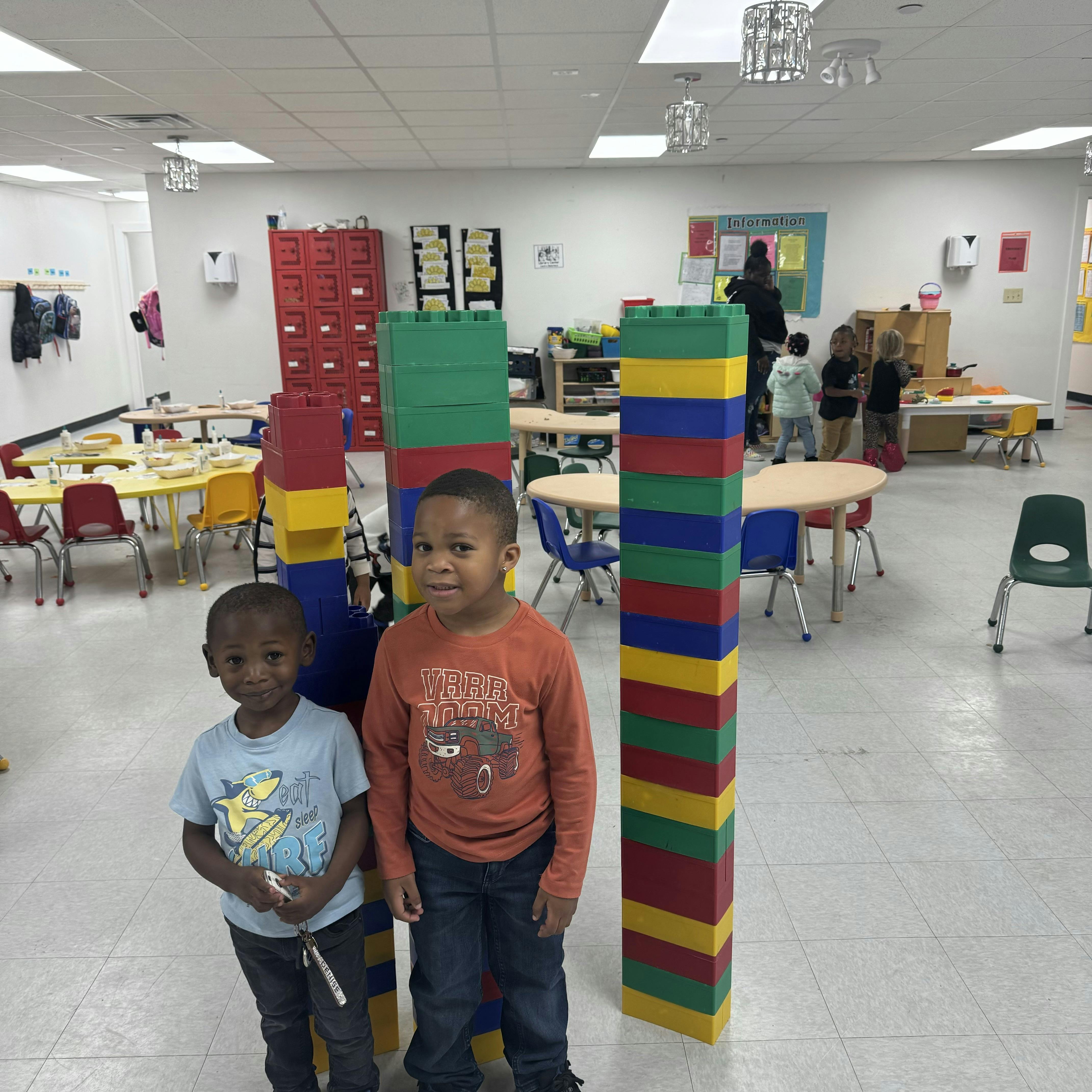 Two children standing next to large colorful blocks in a classroom