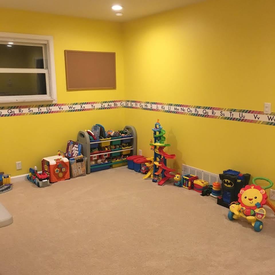 Playroom with yellow walls, alphabet border, and various toys on the floor
