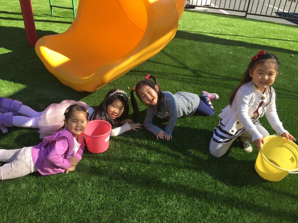 Four children playing on grass with buckets near a slide