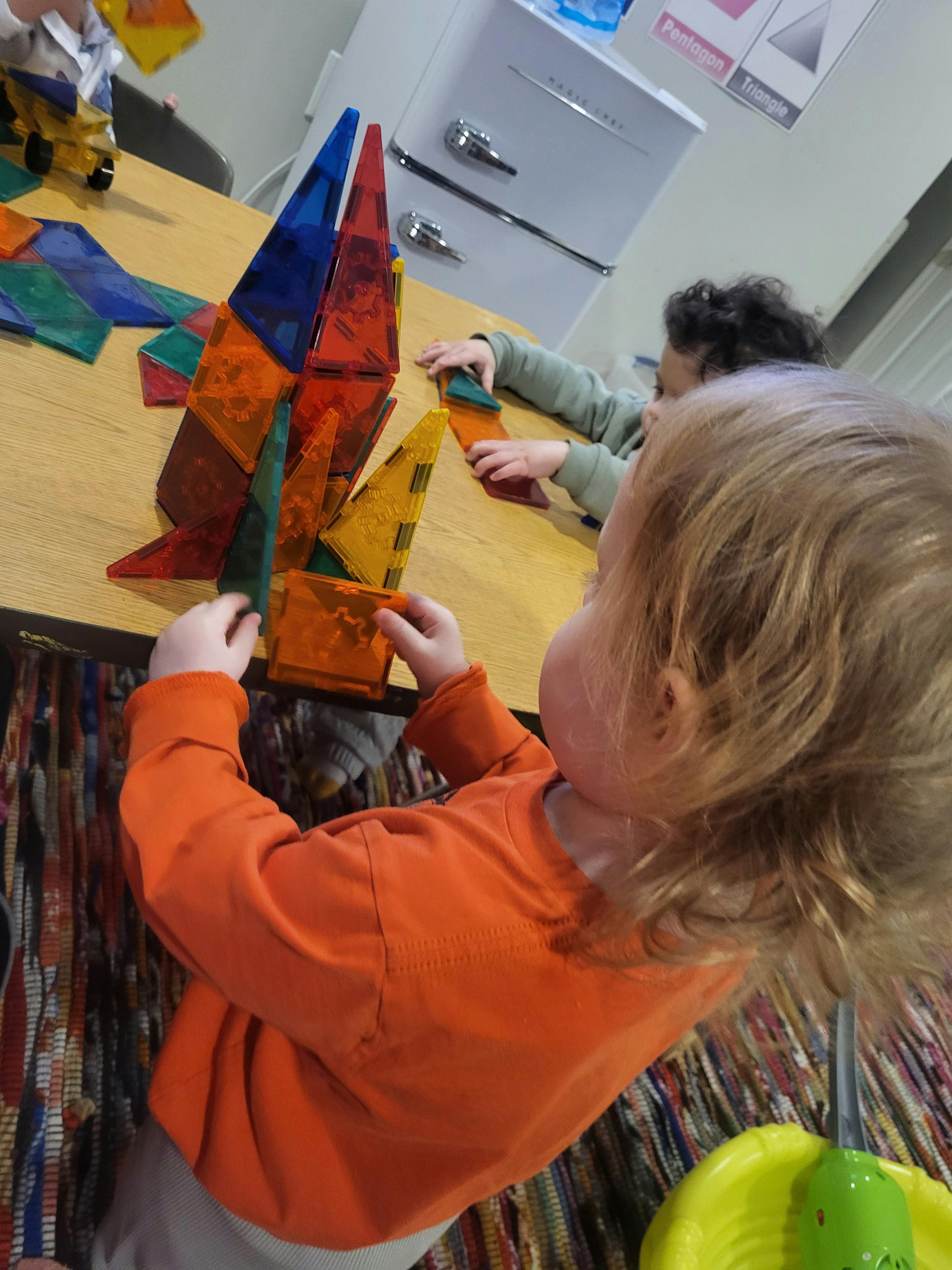 Child playing with colorful magnetic building tiles at a table