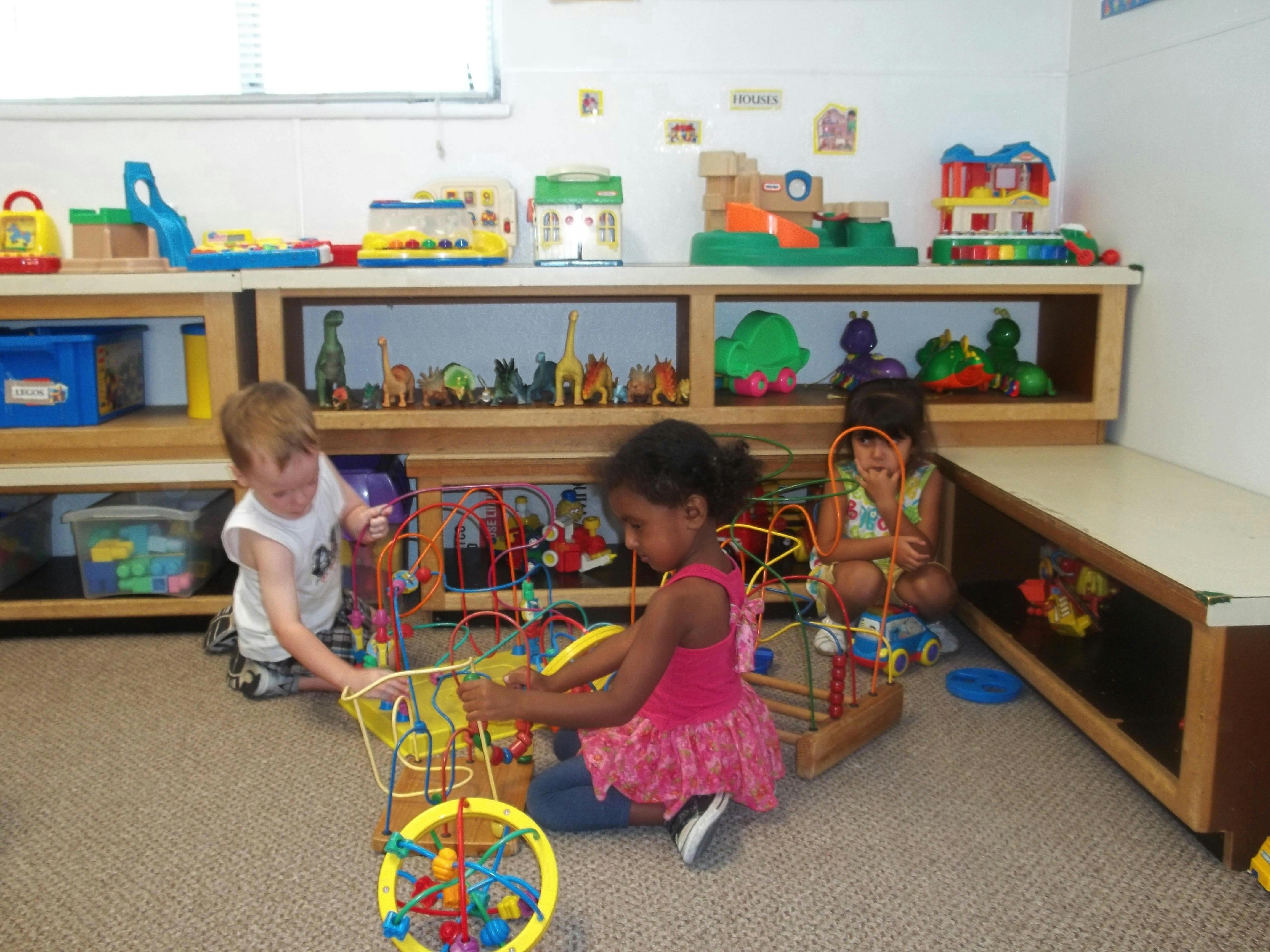 Three children playing with bead maze toys on the floor
