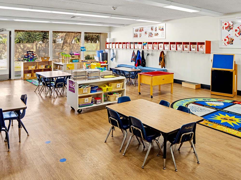 Classroom with small tables and chairs, shelves, and coats hanging on hooks