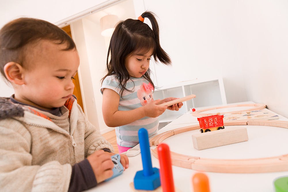 Two children playing with wooden toys and a train set