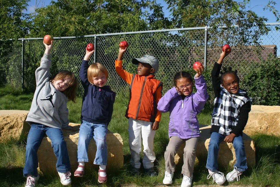 Five children holding apples above their heads outdoors