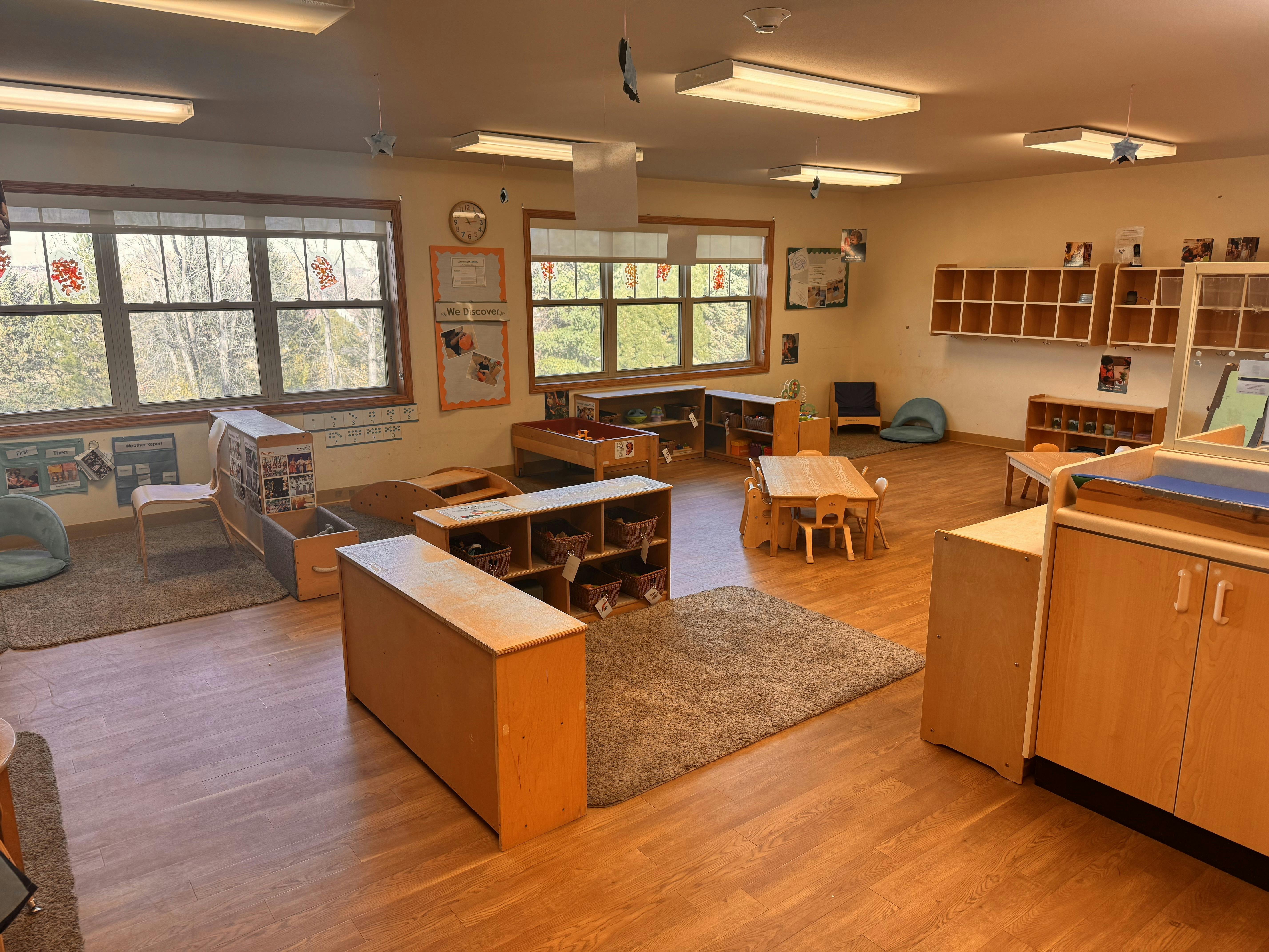 An empty early childhood classroom with multiple windows and learning stations