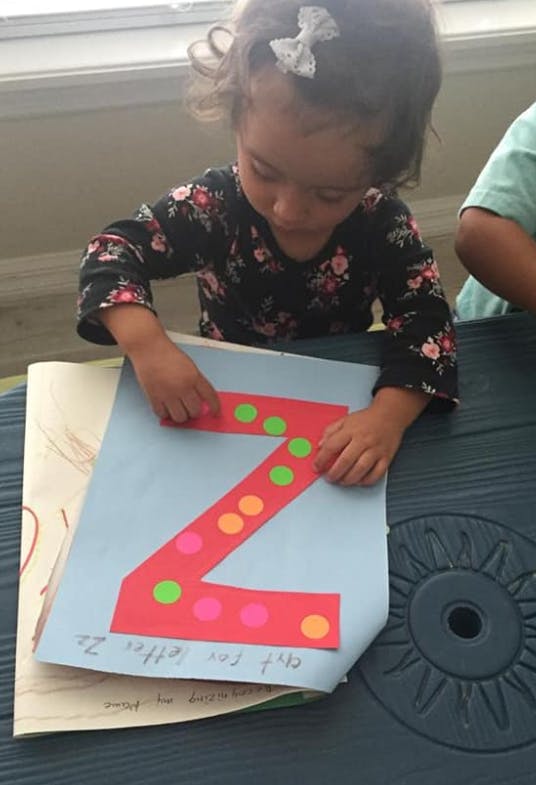 Child decorating a large red letter Z with colorful dots