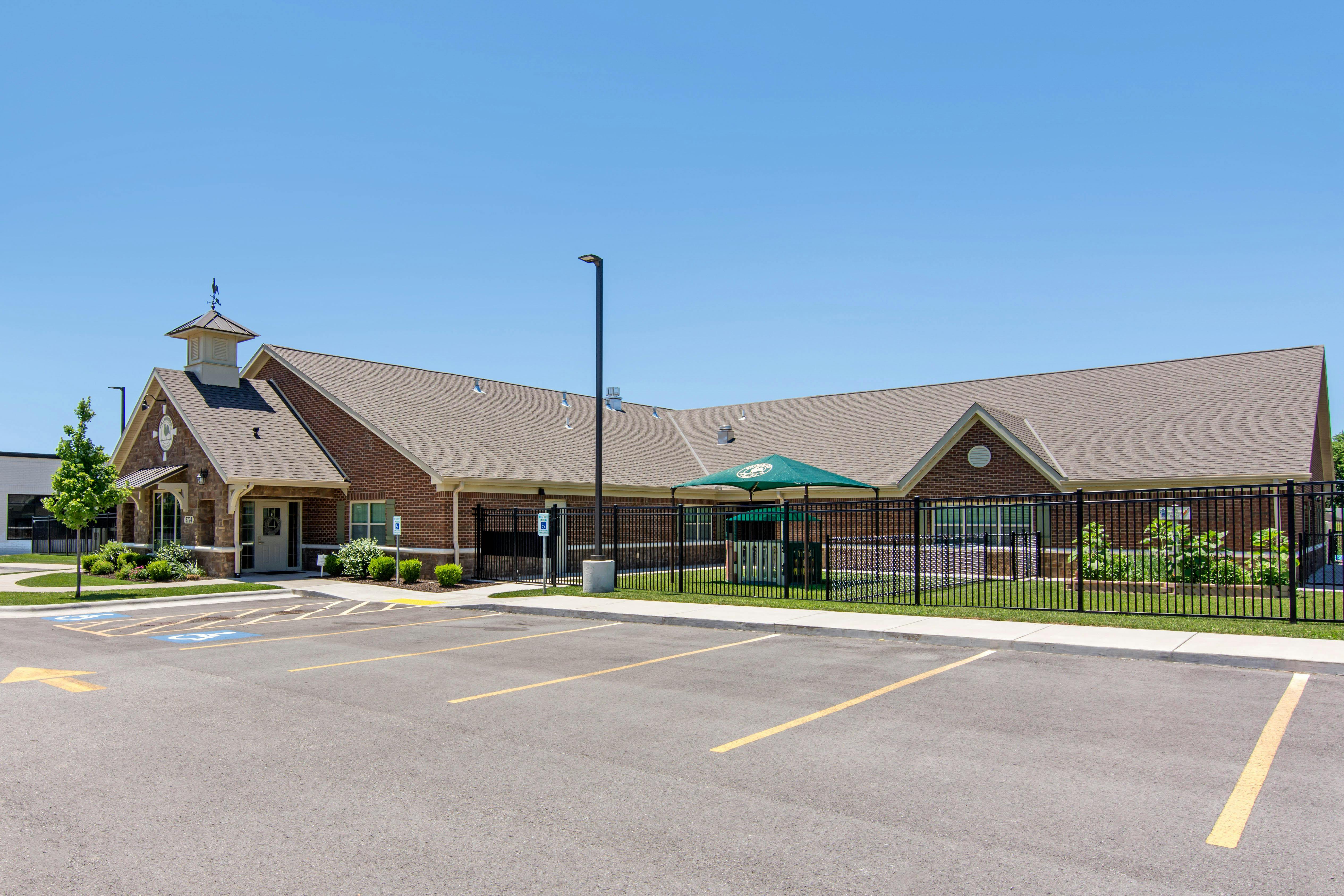 Building with brick facade, cupola, parking lot, and fenced-in playground