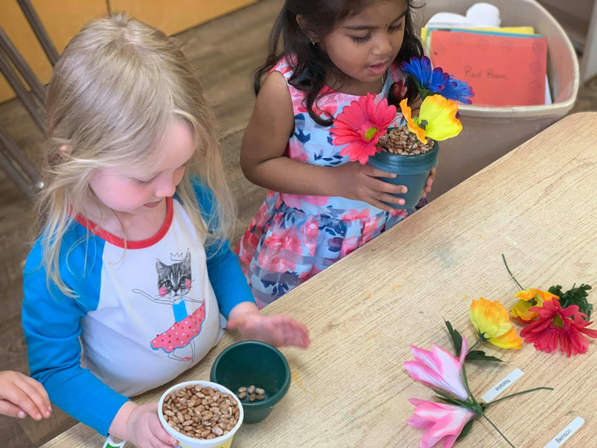 Two children at a table with craft flowers and small containers