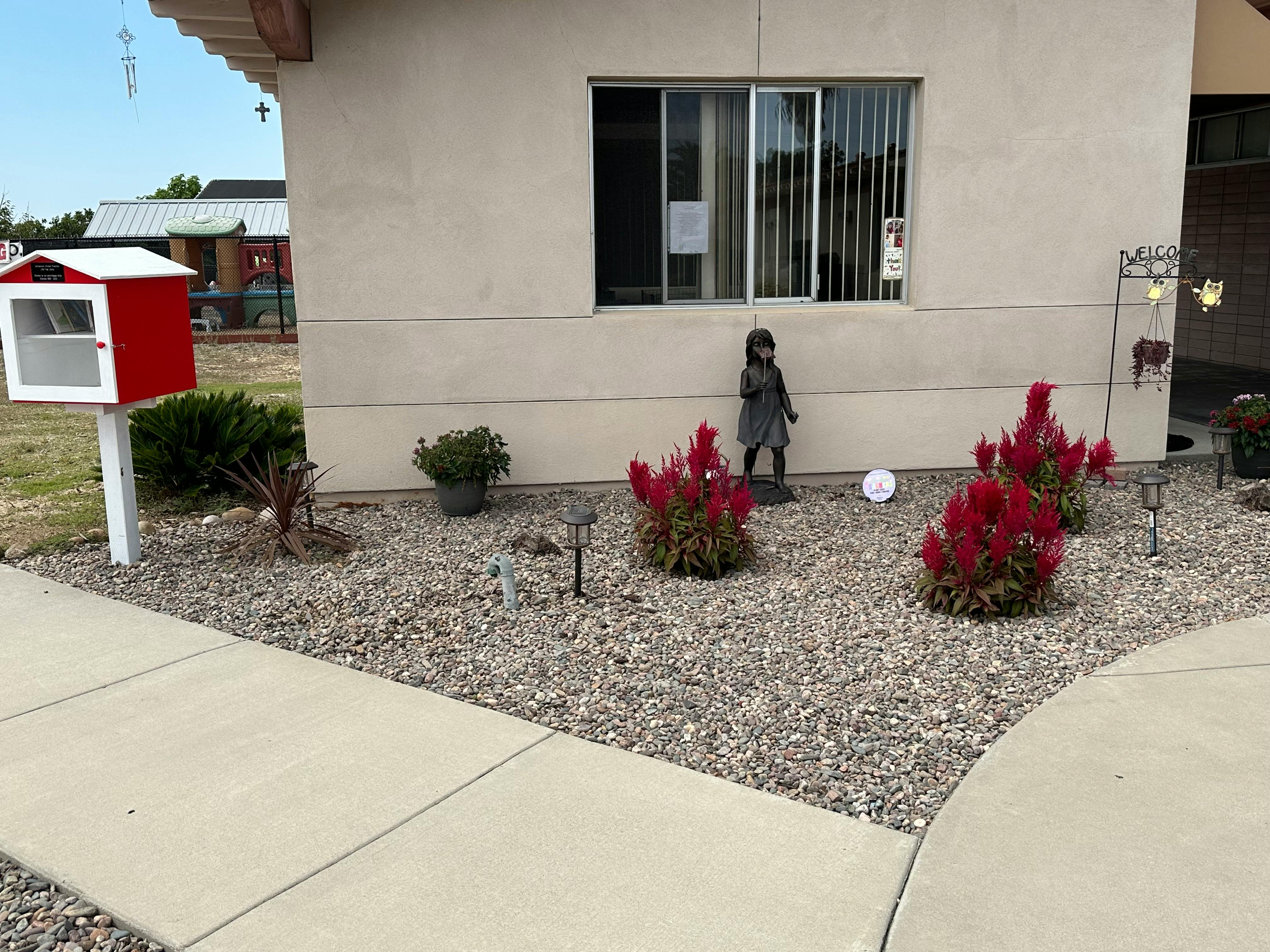 Red and white little free library next to a building with red bushes