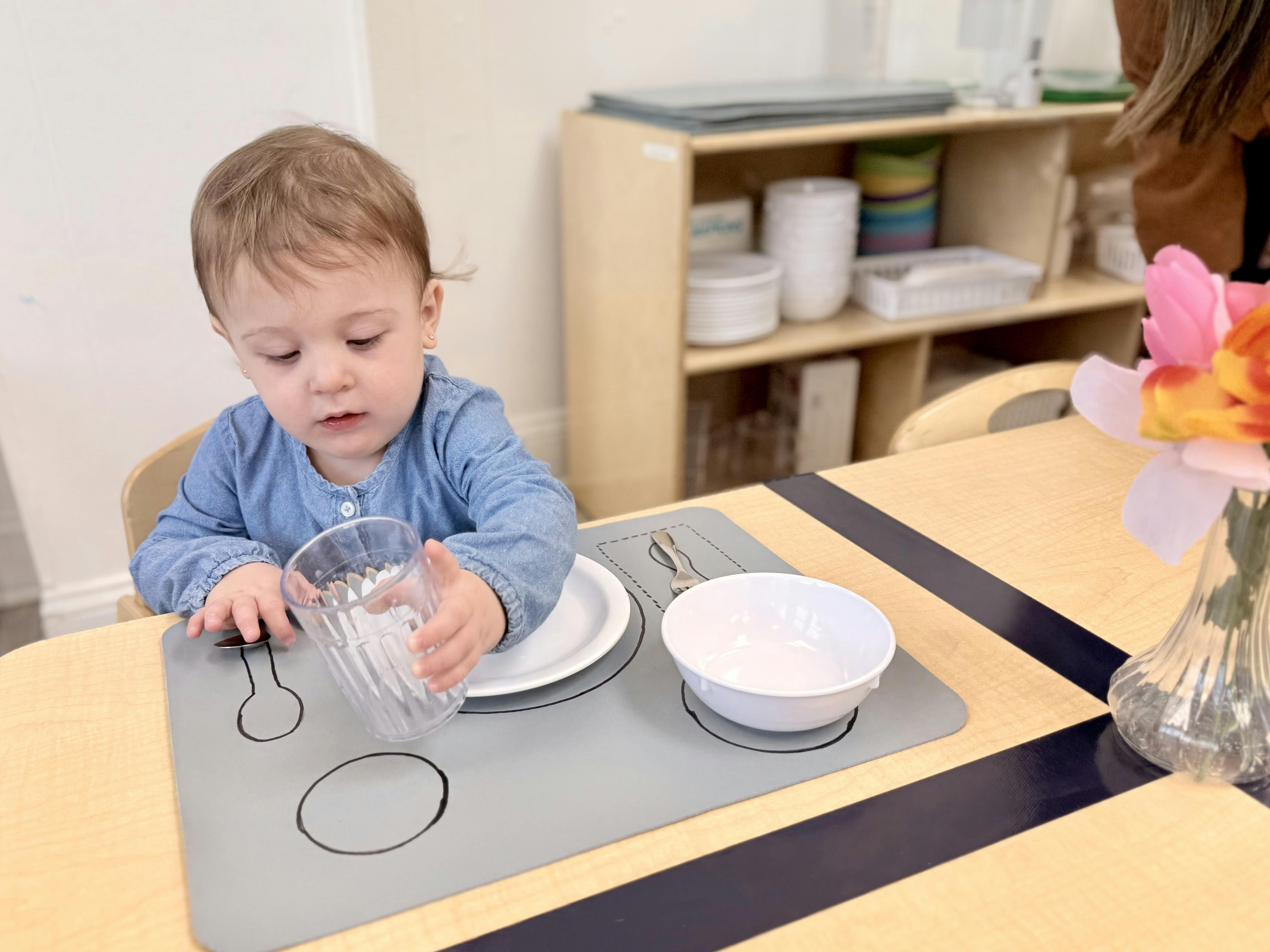 Child sitting at a table with a placemat, plate, bowl, and cup