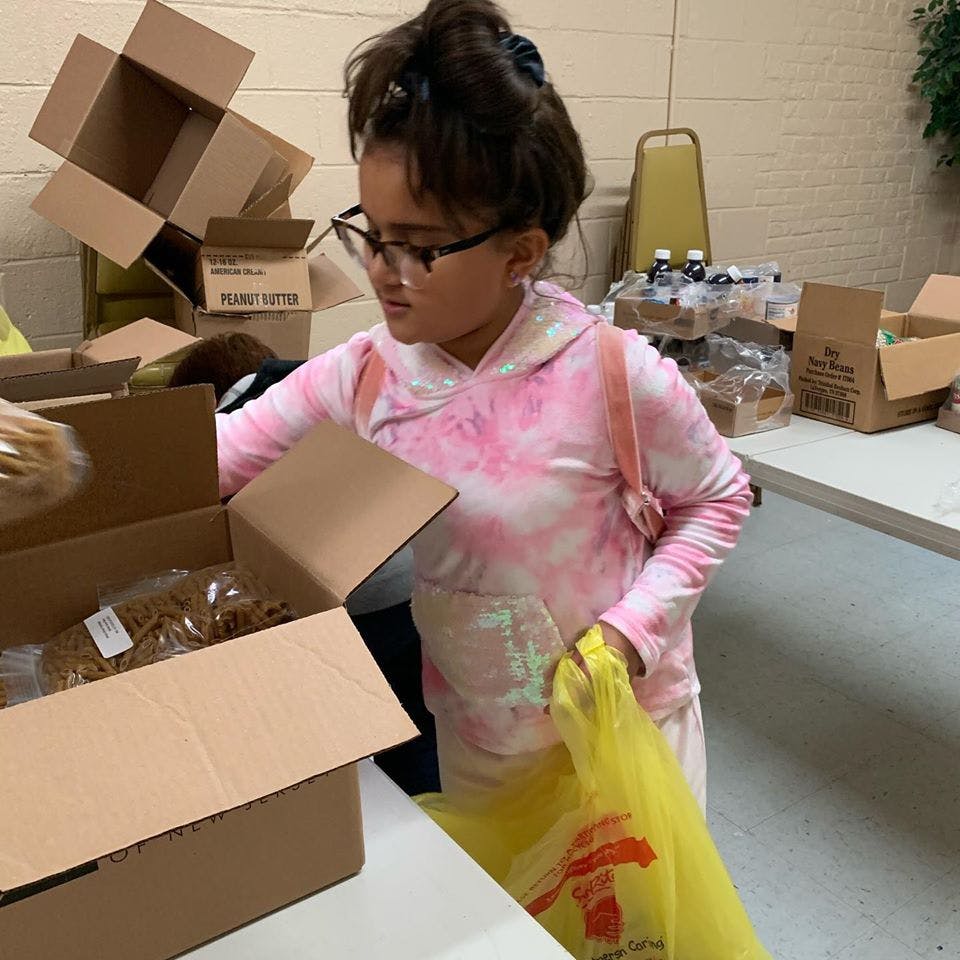 Child in glasses and pink hoodie packing items into a box