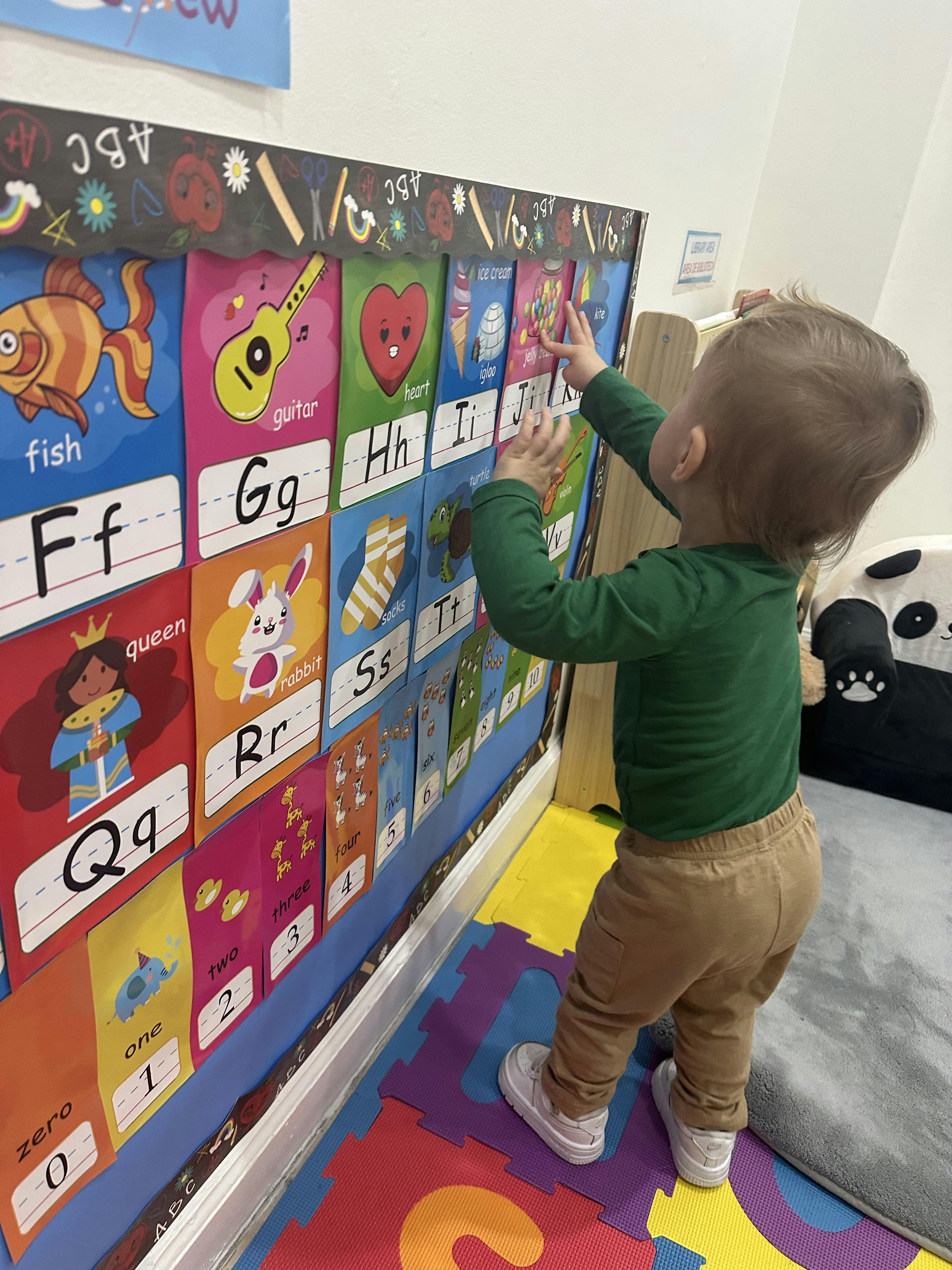 Child reaching towards an alphabet and numbers chart in a classroom