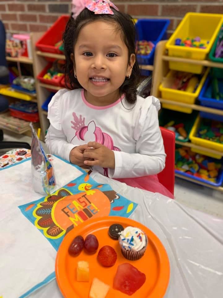 Child sitting at a table with a plate of fruit and a cupcake