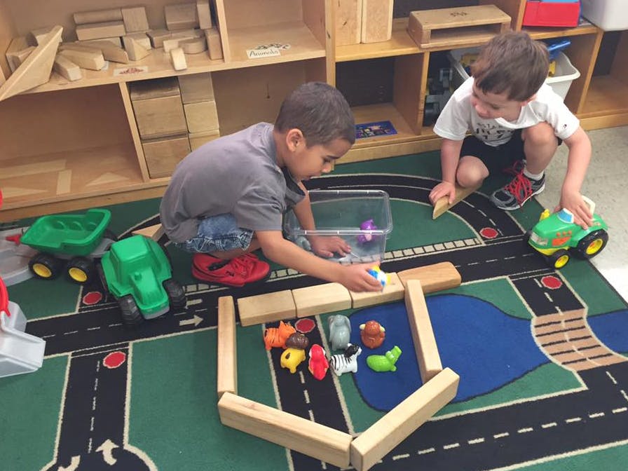 Two children playing with blocks and toy cars on a road-themed rug
