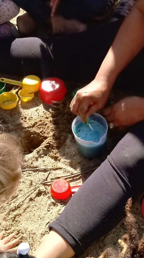 Person stirring blue liquid in a cup in the sand with toys