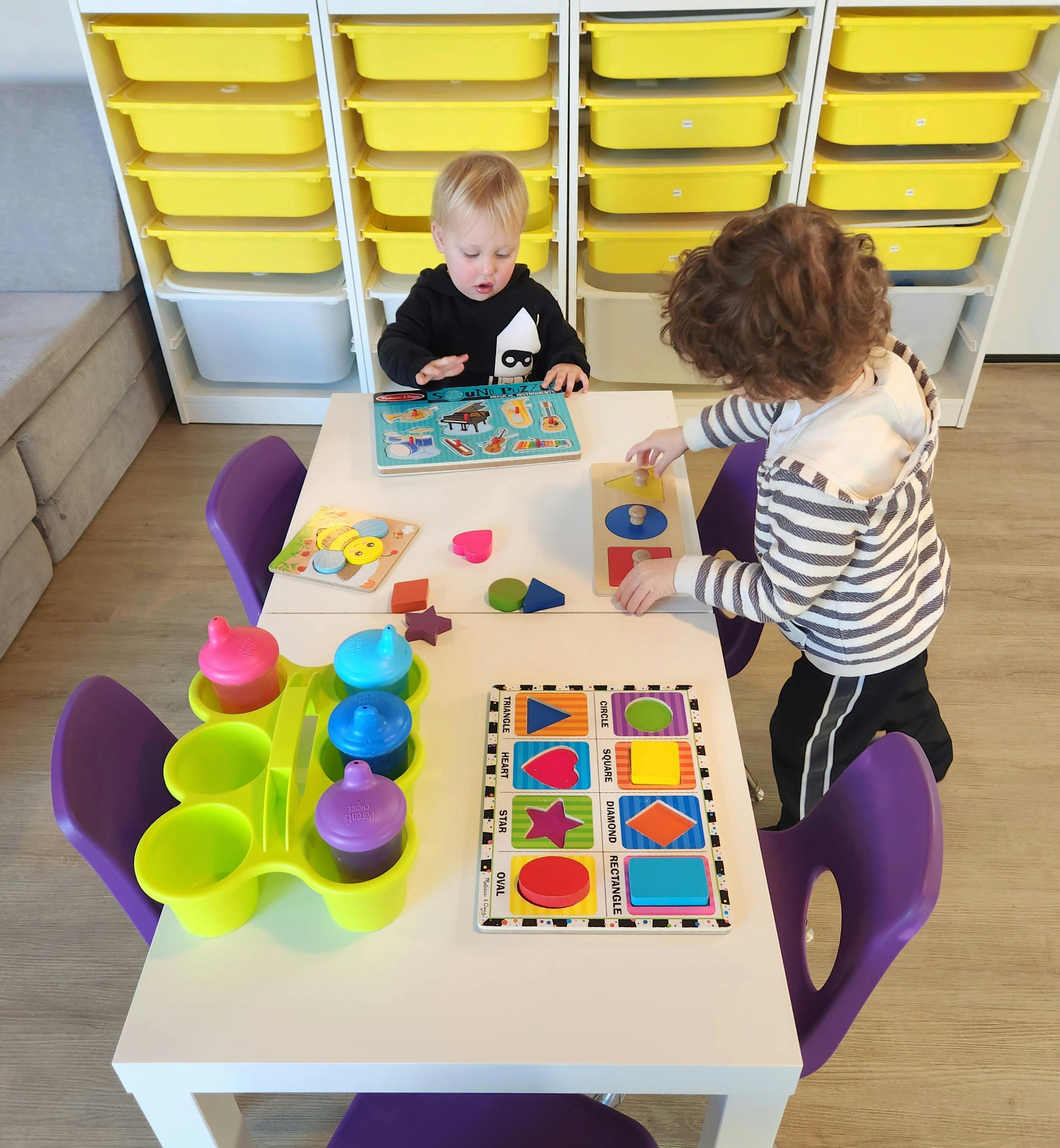 Two children playing with puzzles and toys at a table