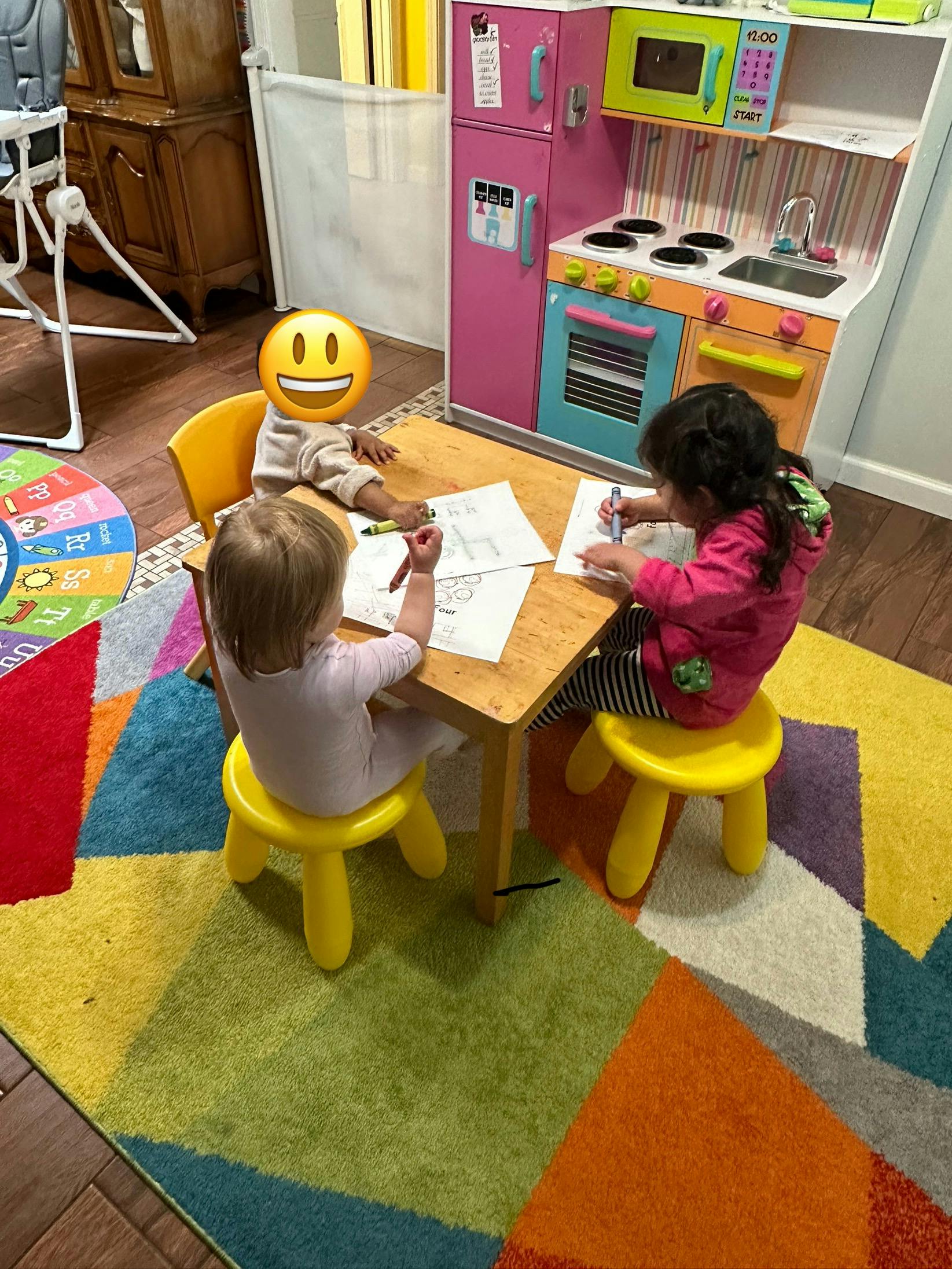 Three children drawing at a small table in a play area