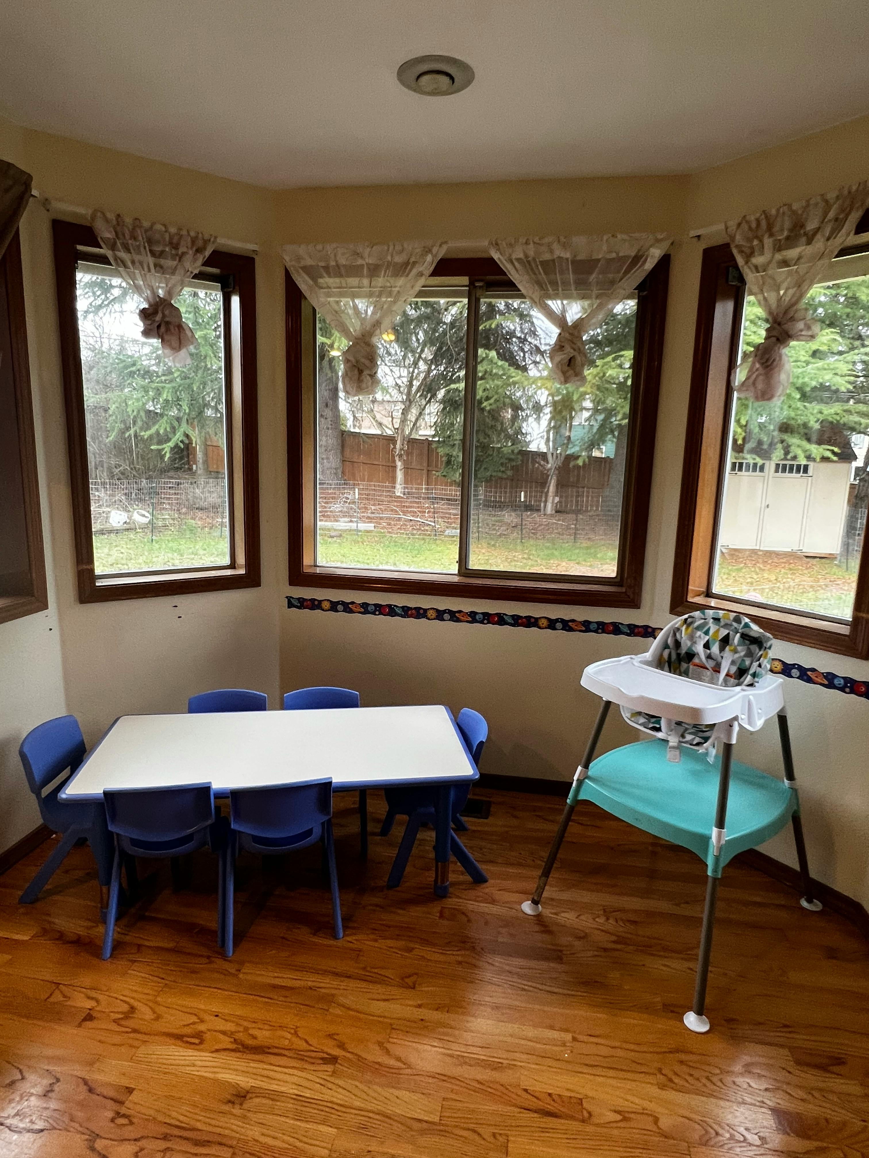 Children's table with blue chairs and a high chair in a room with windows