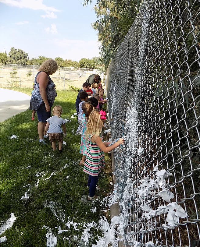 Adult and children playing with foam on a chain link fence