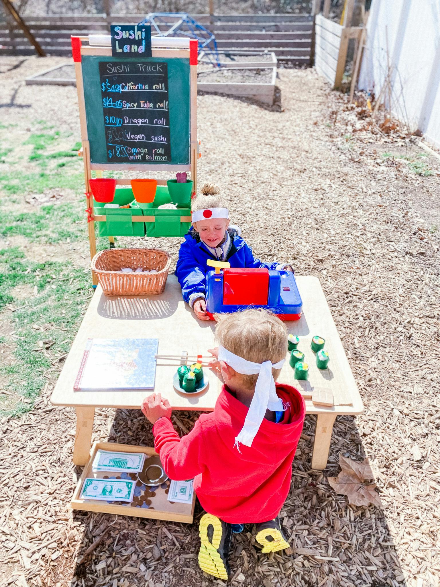 Two children playing with a toy sushi stand outdoors