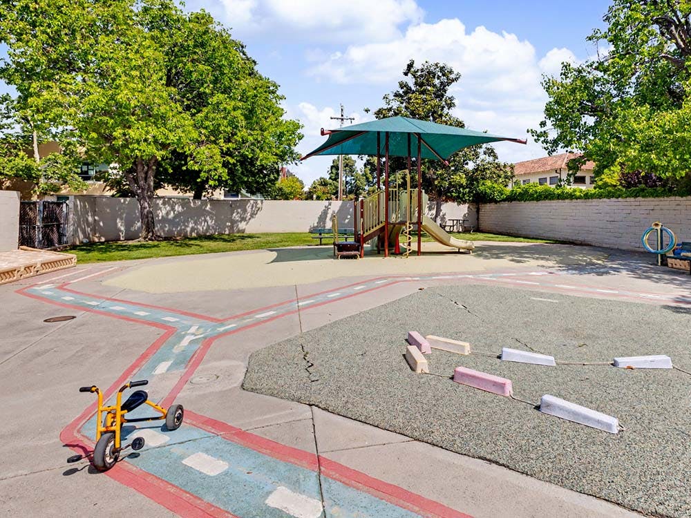 Playground with a yellow tricycle on a painted road and a slide under a canopy