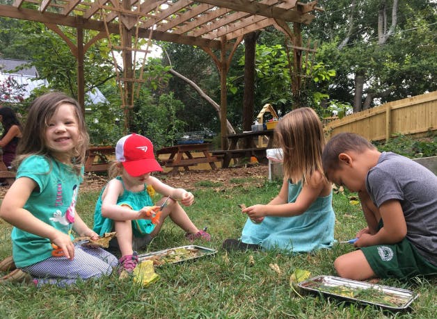 Four children sitting on grass with trays of natural materials