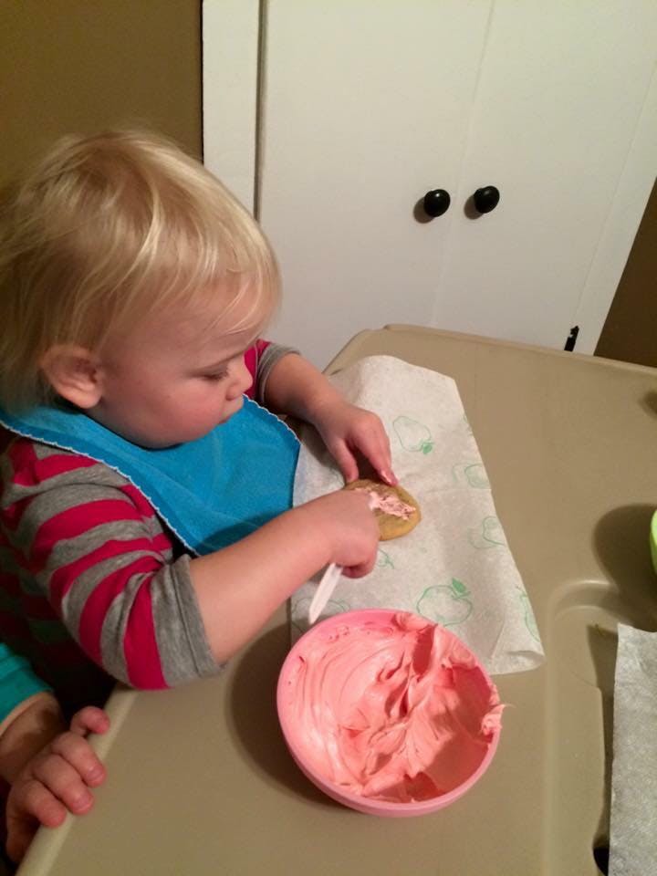 Child in a high chair decorating a cookie with pink frosting