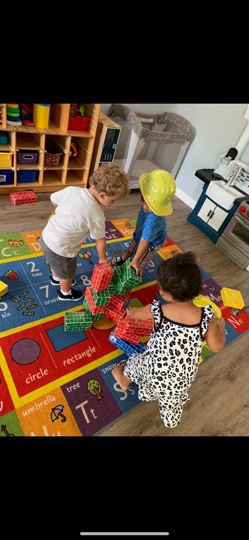 Three children playing with blocks on a colorful rug