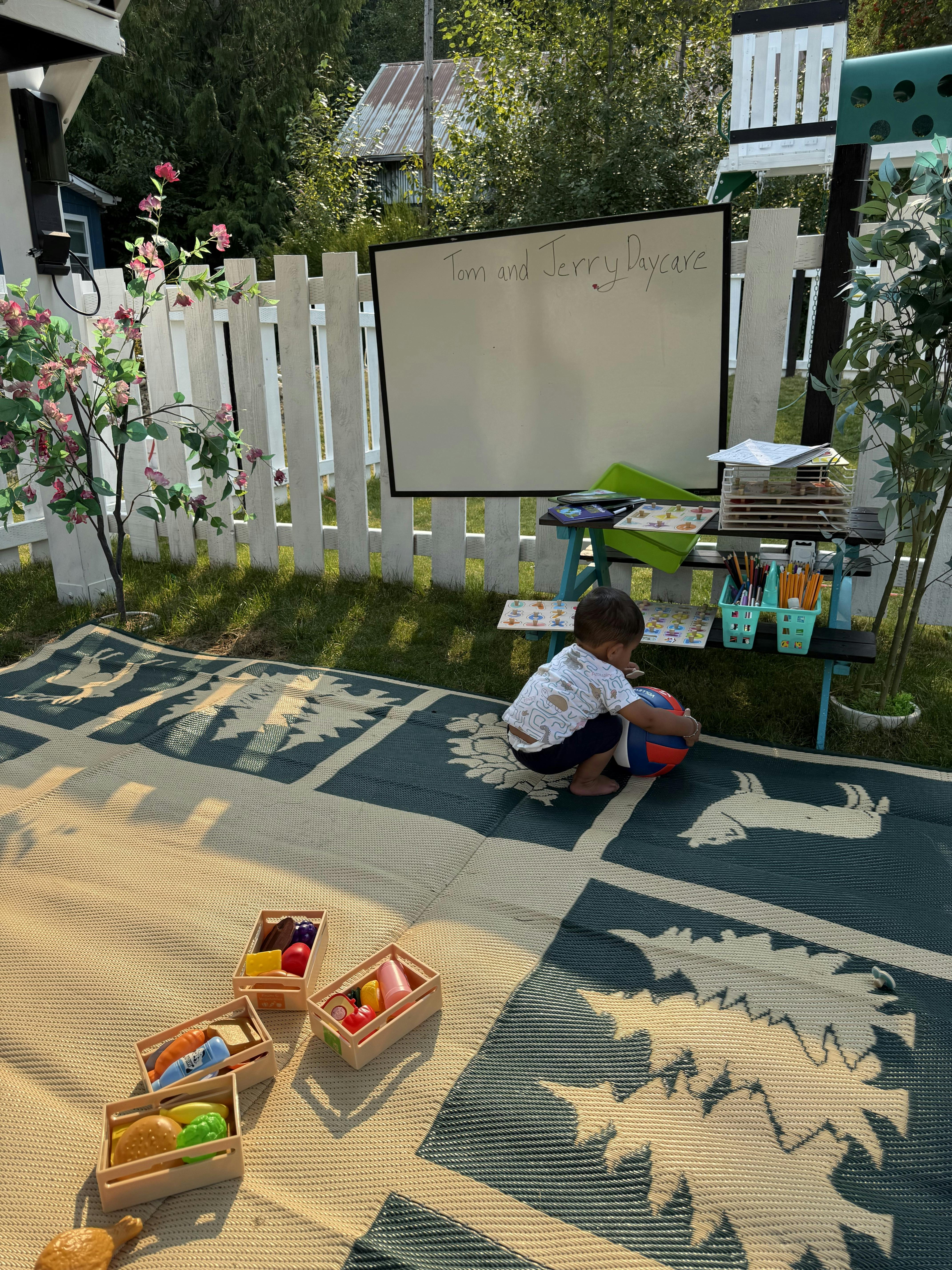 Child playing with a ball on an outdoor play mat by a whiteboard