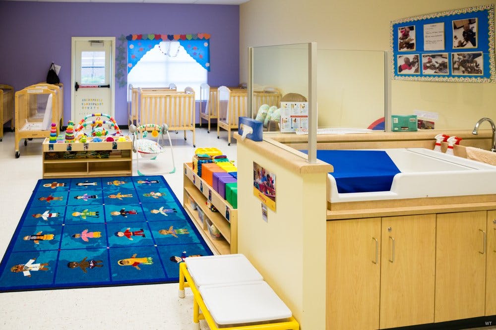 Daycare room with cribs, changing table, and play rug