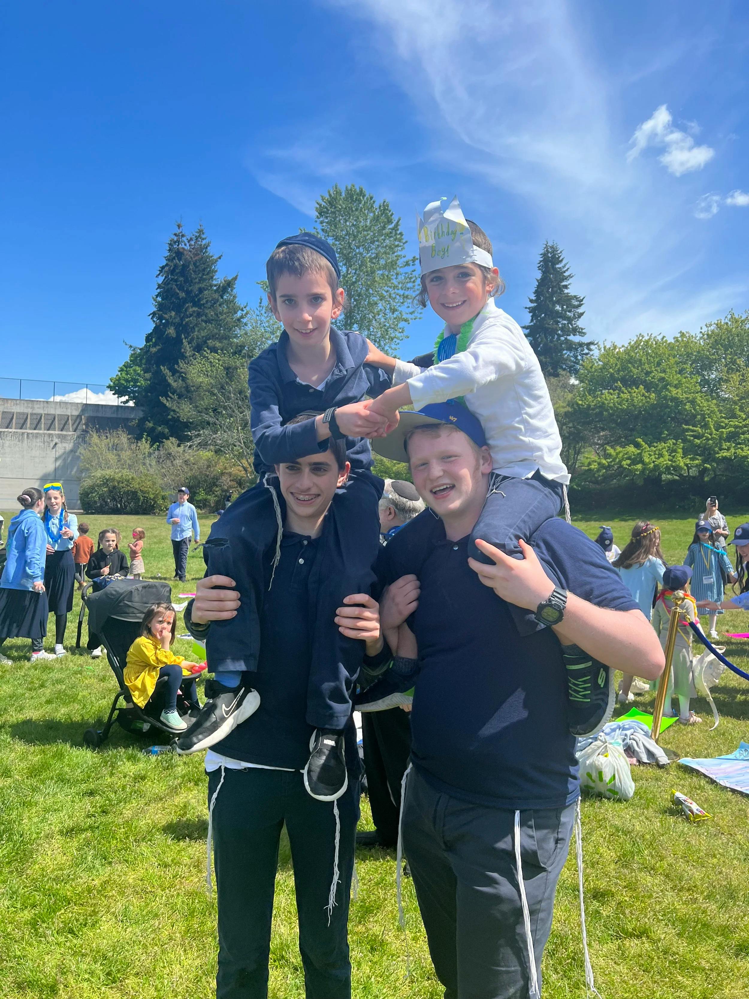 Two people giving piggyback rides to two children, one child wearing a "Birthday Boy" crown