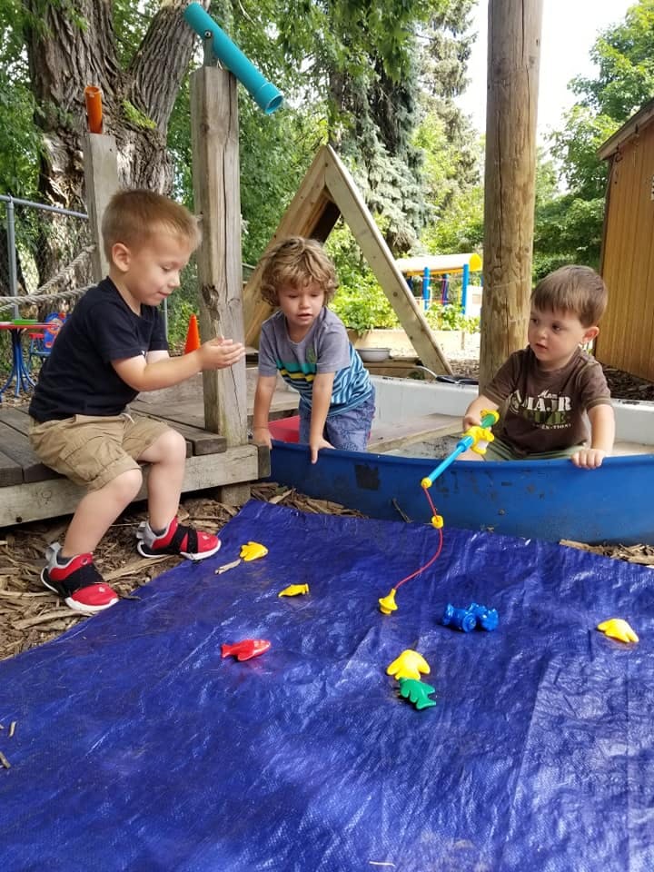 Three children playing with toys on a blue tarp outdoors
