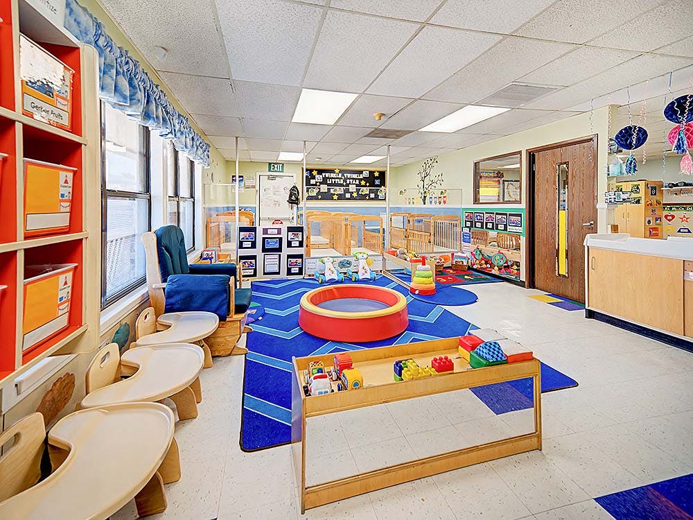 A colorful classroom with cribs, high chairs, a rocking chair, and toys