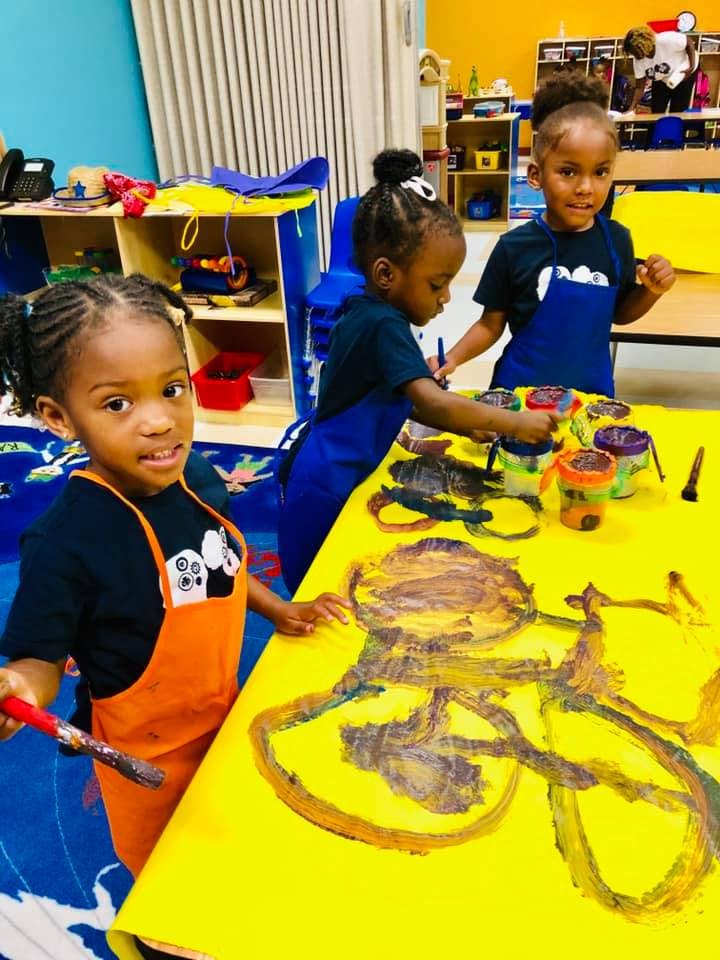 Three children painting at a table in a classroom