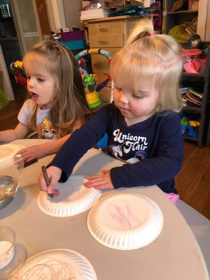 Two children drawing on paper plates at a table