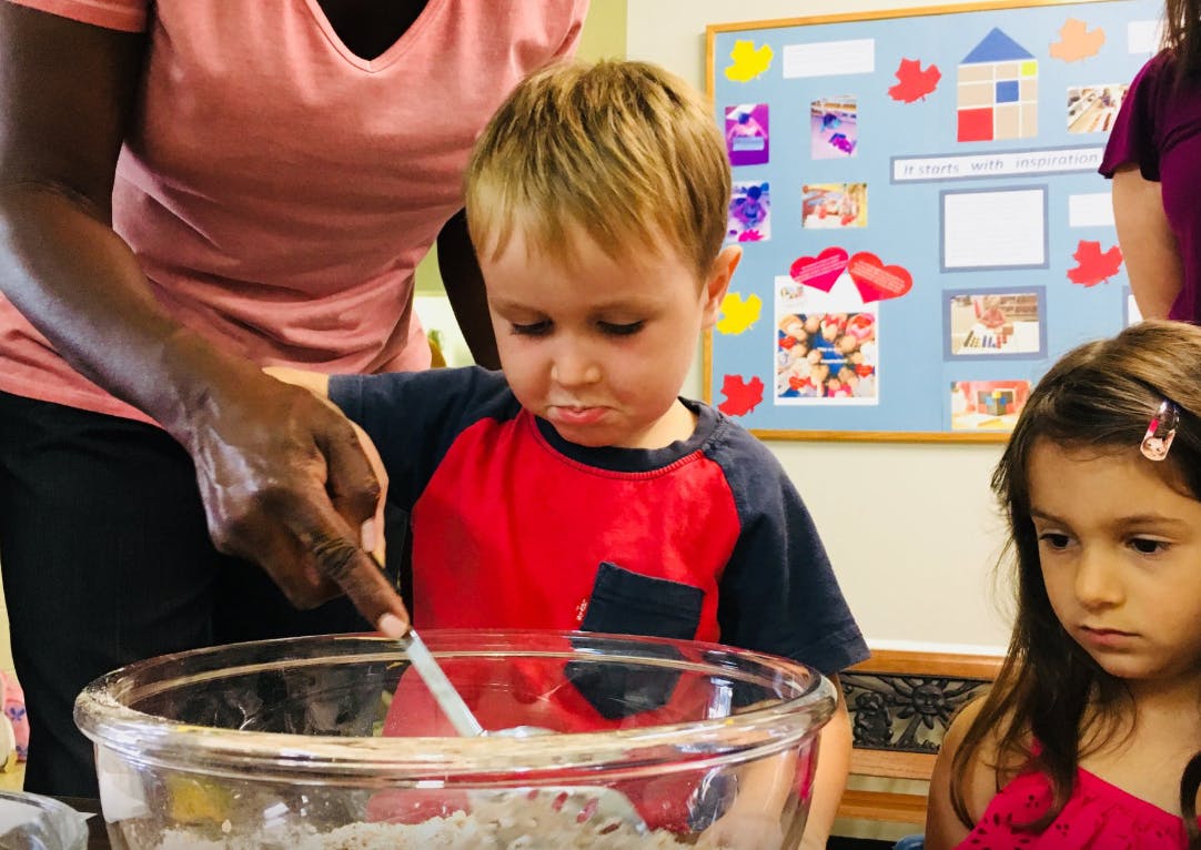 Adult helping a child stir a bowl in a classroom