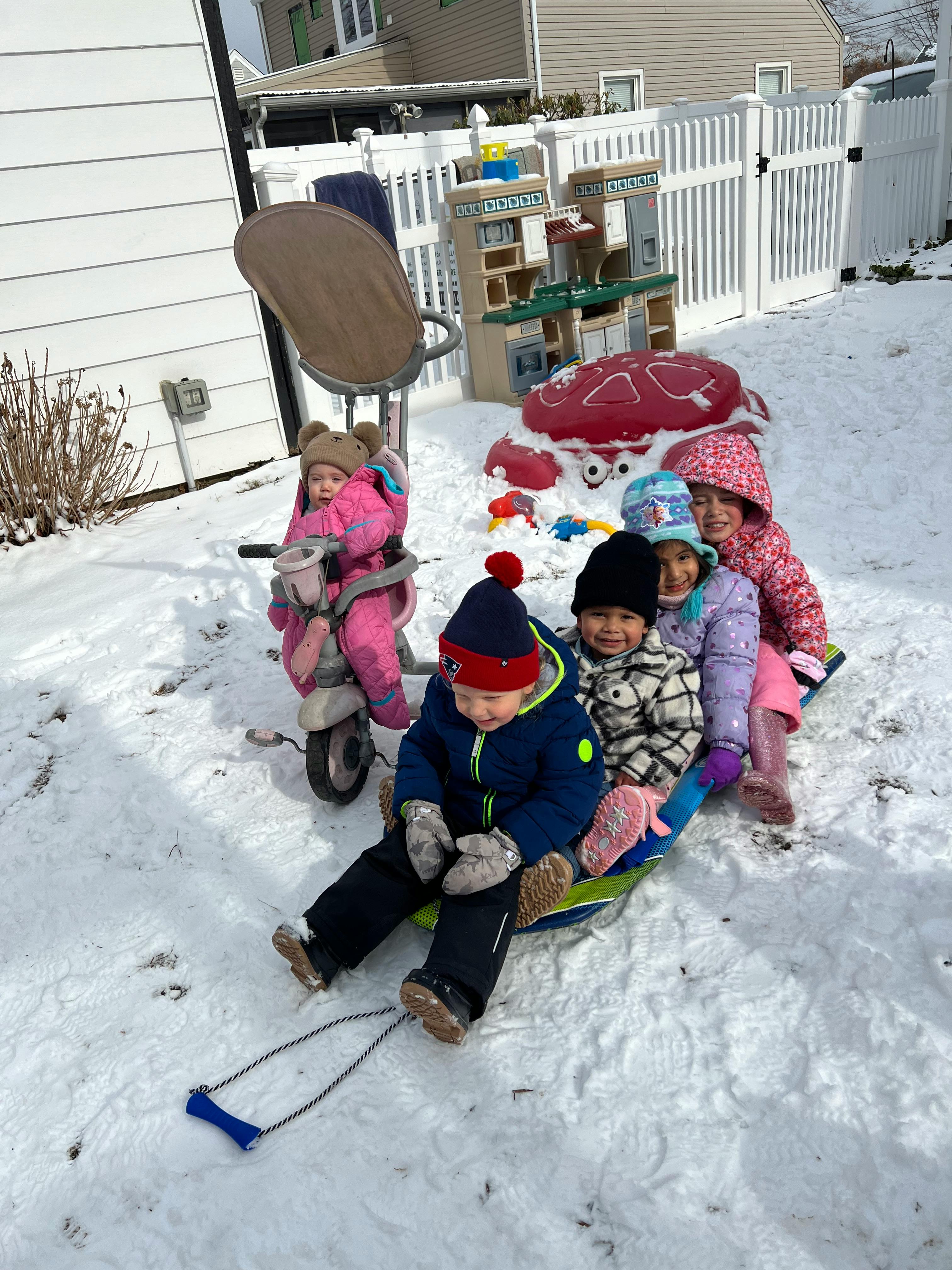 Children playing in the snow, one on a tricycle, others on a sled