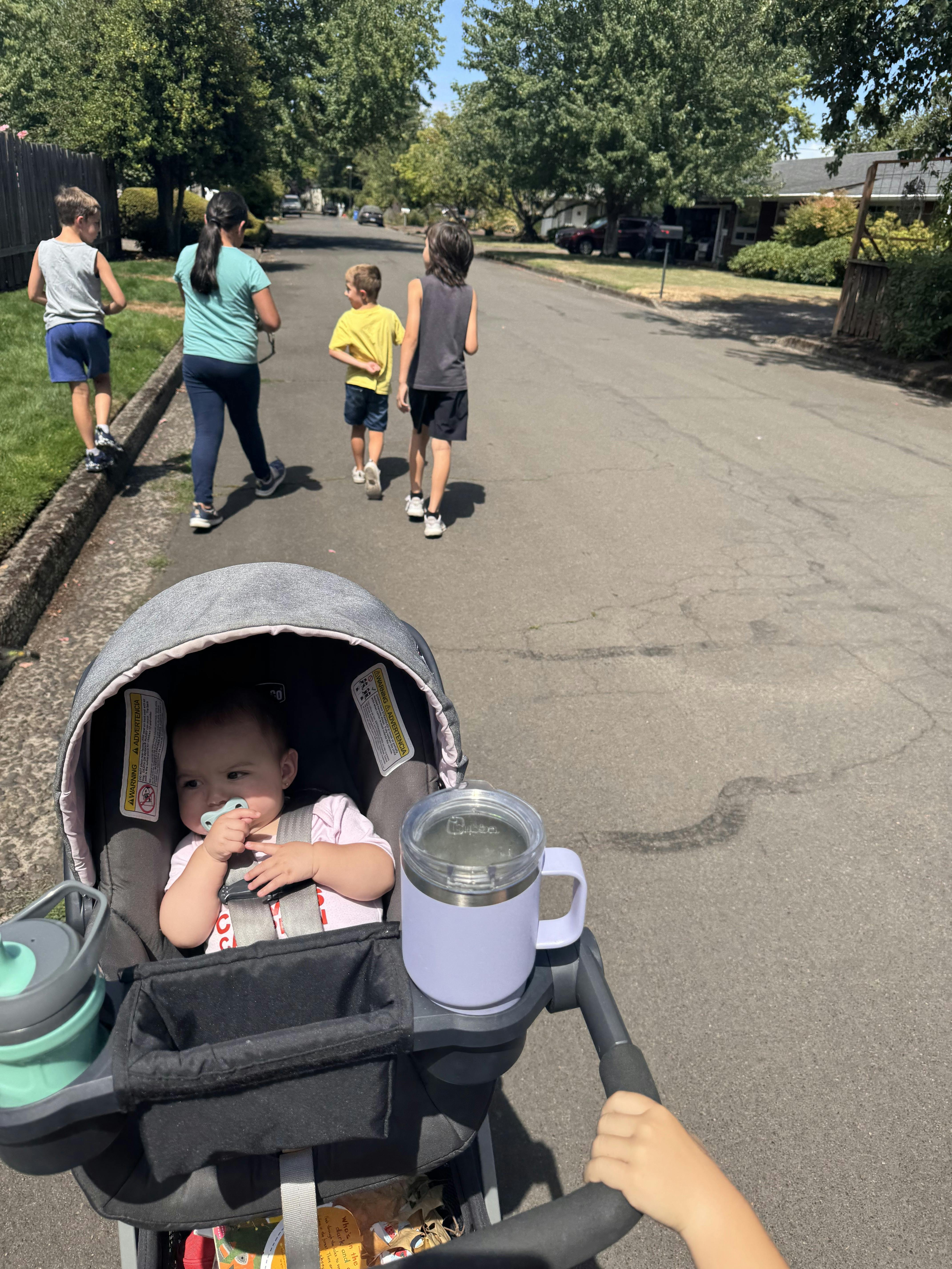 Baby in a stroller with children walking ahead on a street