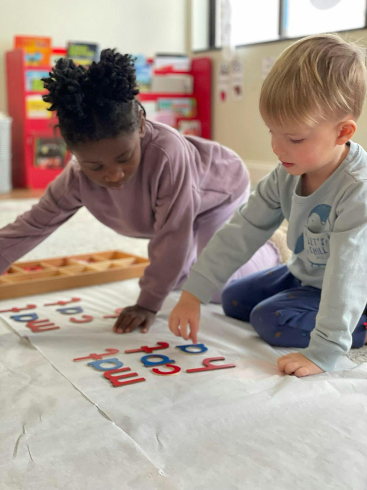 Two children playing with letter tiles on the floor