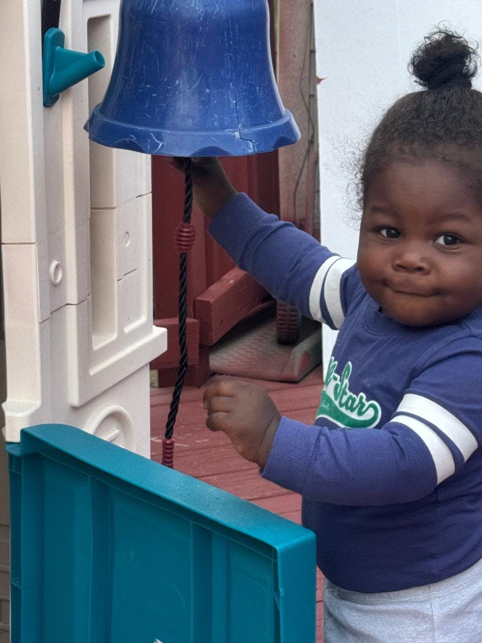 Child playing with a blue toy bell on a playground