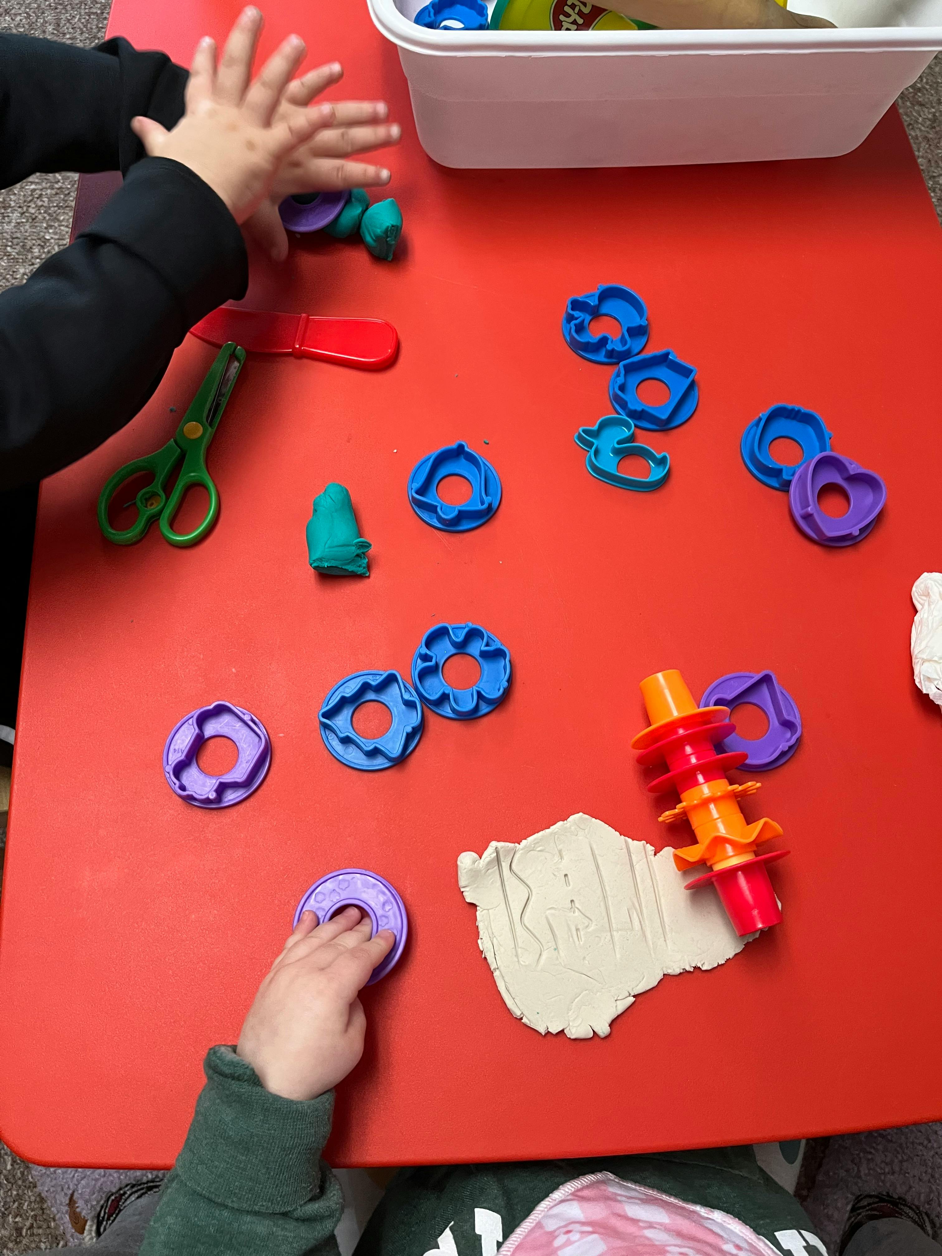 Child's hands playing with modeling clay and cookie cutters on a red table