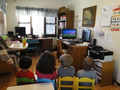 Three children sitting in chairs facing away from the camera in a room
