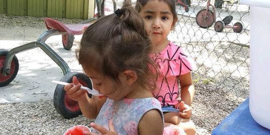 Child eating with a spoon, another child sitting behind